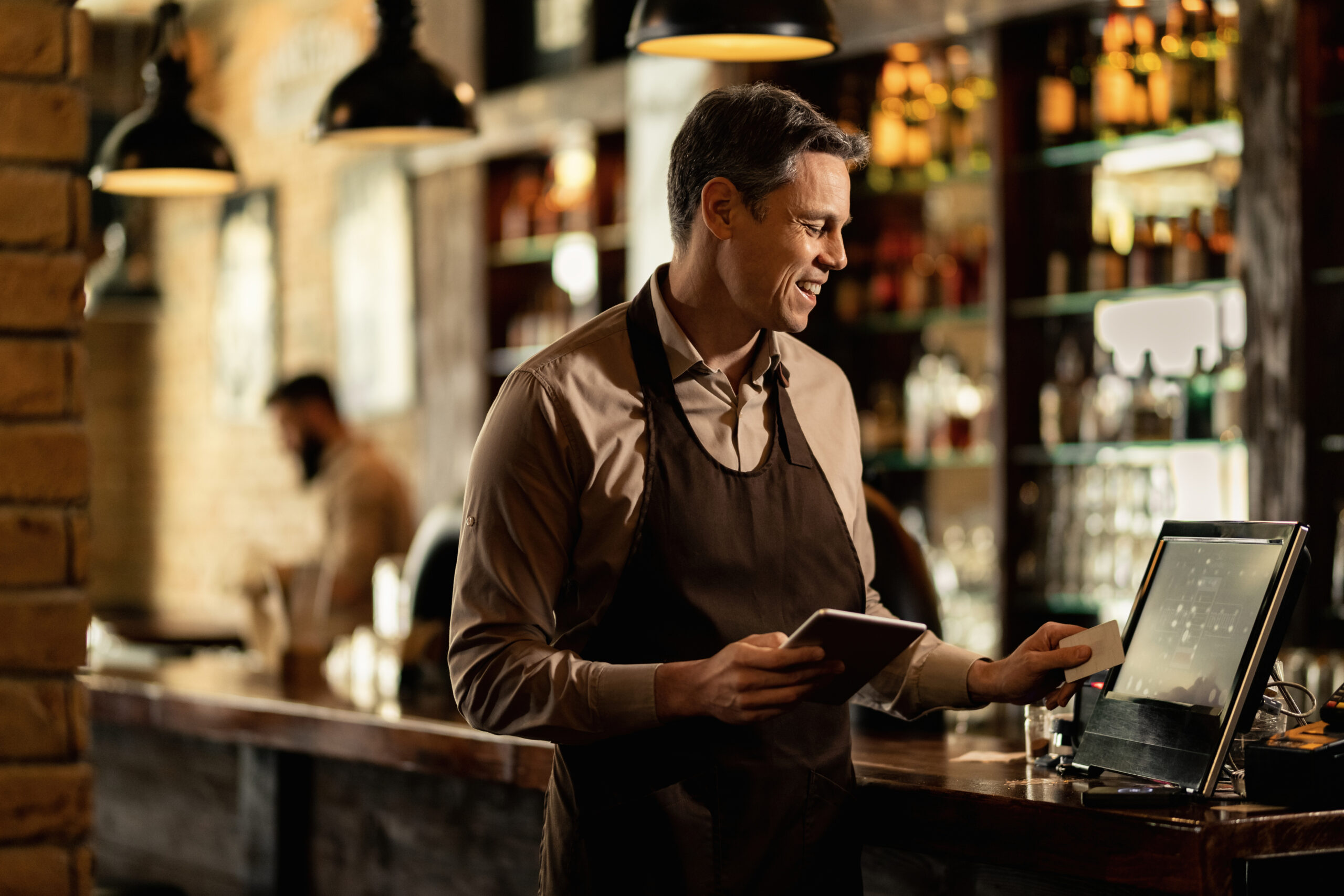Happy waiter working at cash register in a bar.